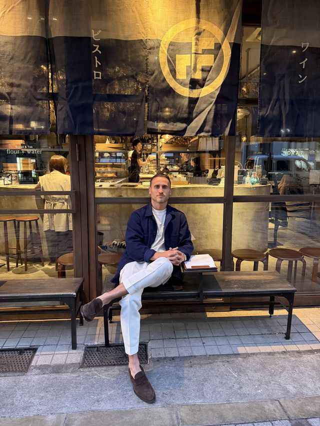 Me on a bench outside a bistro in Japan, in a navy jacket and cream trousers