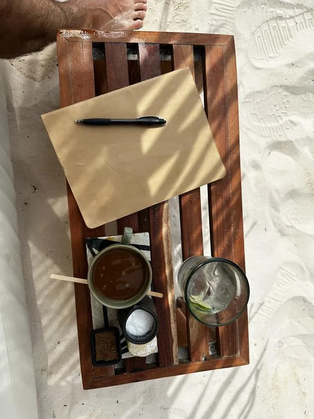 A tray with a notepad, pen and espresso on a beach table
