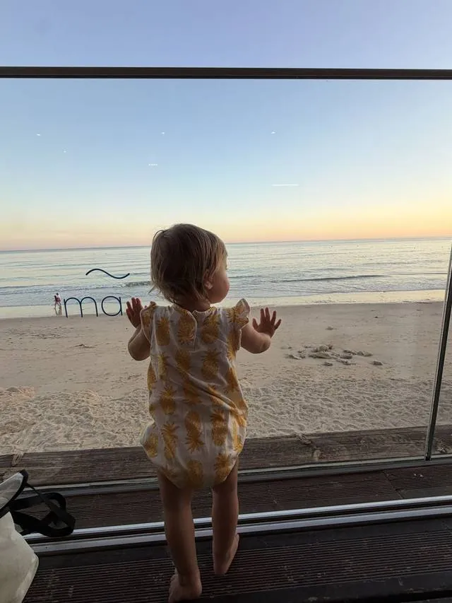 My daughter at a window looking out at the beach at sunset