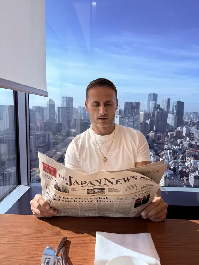 Me reading The Japan News at a window table above the Tokyo skyline